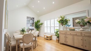 A modern kitchen with wooden cabinets, a dining table with chairs, and a large window with blinds.