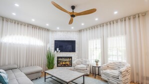 A living room with a sofa, a coffee table, a fireplace, a television, and a ceiling fan.