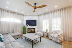 A living room with a sofa, a coffee table, a fireplace, a television, and a ceiling fan.