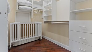 Ein begehbarer Kleiderschrank mit offenen Regalen, einer weißen Kommode und einem weißen Babybett.