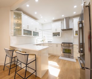 A modern kitchen with white cabinetry, a central island, stainless steel appliances, and a bar stool seating area. - 2 short blocks  to the beach. FULLY RENOVATED HOUSE  WITH NEW HOT TUB. (Point Pleasant Beach)