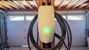 Eine Tesla-Ladestation in einer Garage mit Holzbalken und einer Garagentür im Hintergrund.