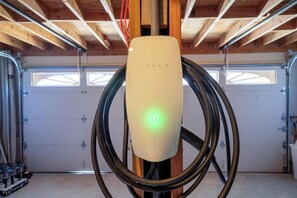 A Tesla charging station in a garage with wooden beams and a garage door in the background.