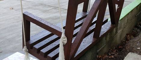 Un banc en bois avec des garde-corps en métal, placé sur une terrasse carrelée bordée de béton.