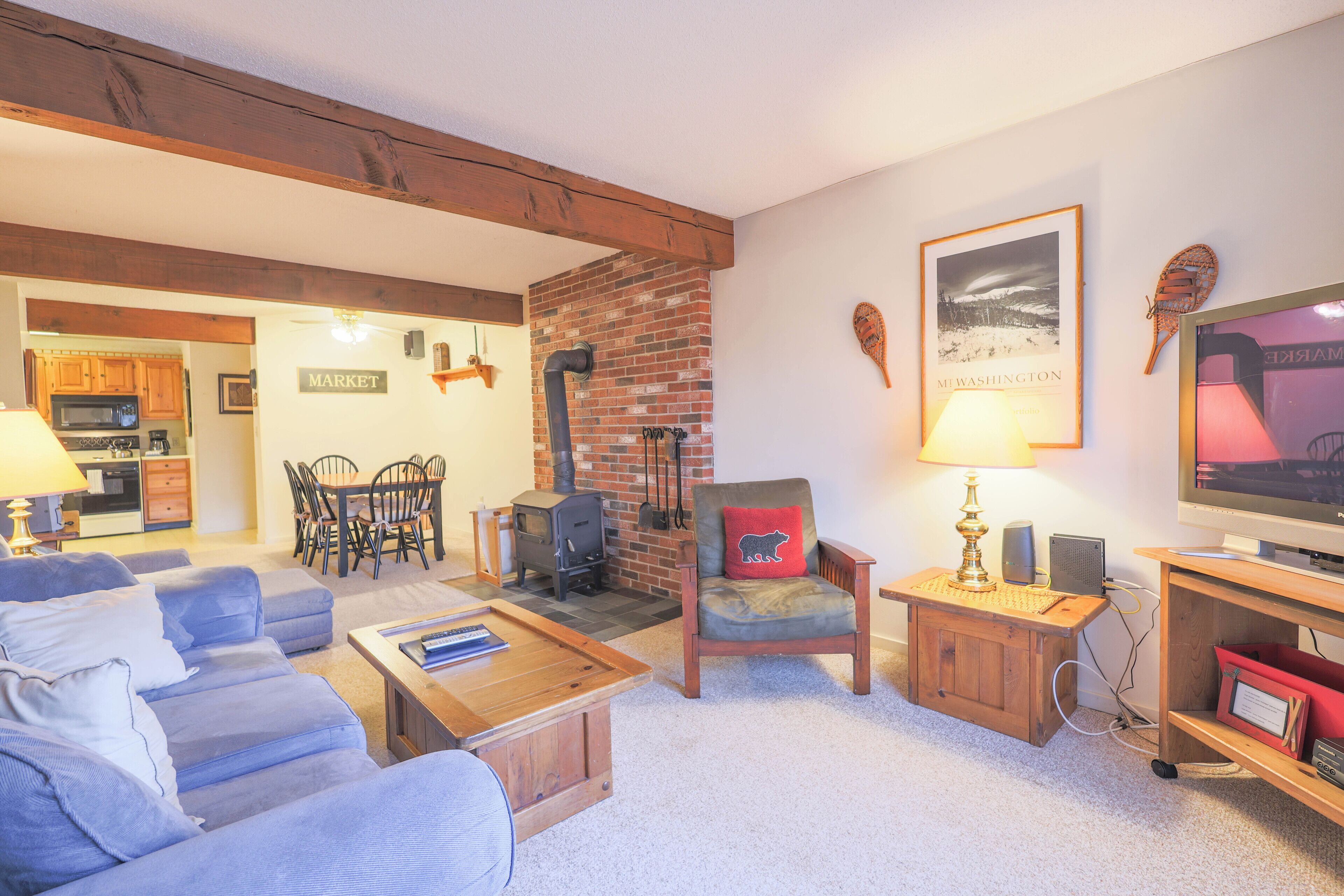 Una sala de estar con sofá, mesa de centro, chimenea, televisor y una cocina al fondo.