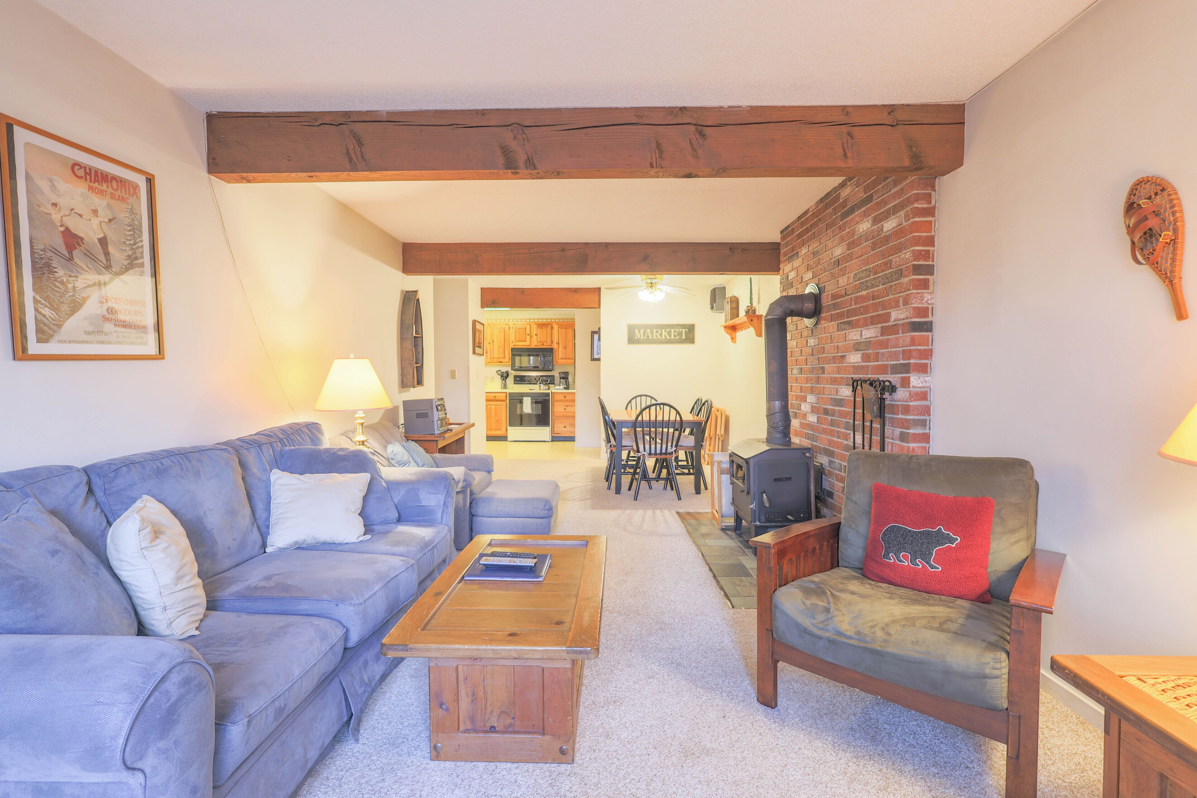 Een woonkamer met een blauwe bank, een houten salontafel, een leren fauteuil met een knuffelkussen, en een bakstenen muur.