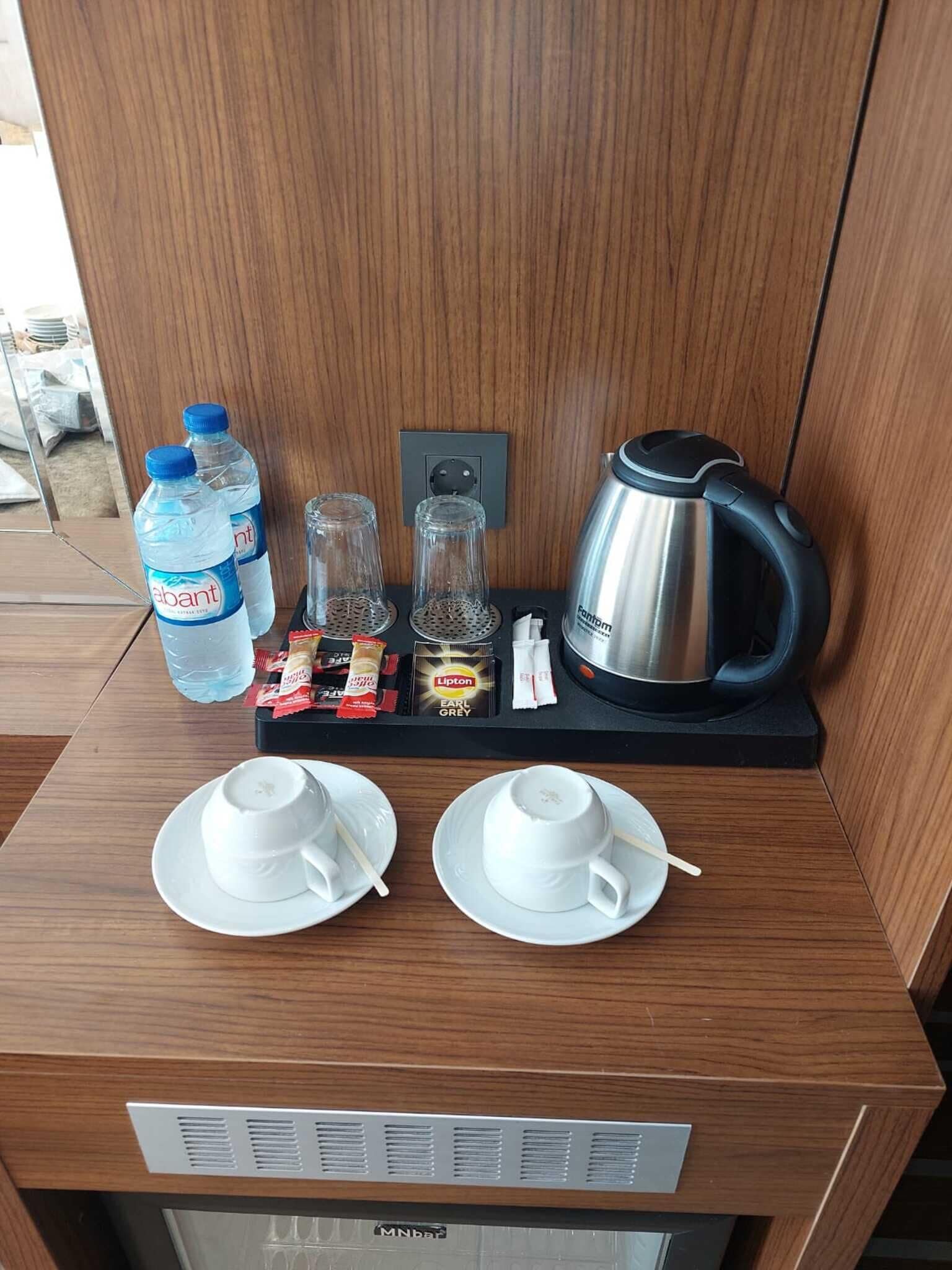 A hotel room's breakfast setup with two white cups, two water bottles, a kettle, and a tray with tea bags and snacks.
