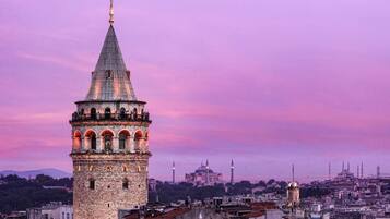 A historic tower with a conical roof and multiple arches, overlooking a cityscape with a prominent mosque in the background.