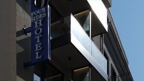 Ein Hotelschild mit der Aufschrift "Four Sides Hotel" vor einer modernen Gebäudefassade.