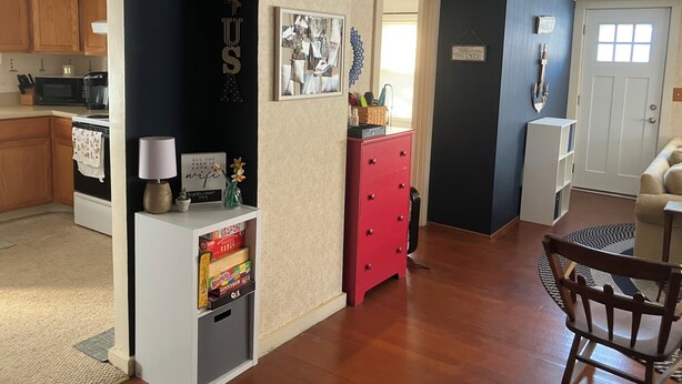 Eine Küche mit Holzausstattung, einer Mikrowelle und einer Kaffeemaschine. Es gibt einen roten Schminktisch und einen weißen Schrank mit Lampe und einem gerahmten Bild.