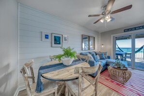Interior de una casa de playa con comedor, un conjunto de sofás y vista al mar a través de amplios ventanales.