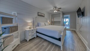A bedroom with a bed, nightstands, a ceiling fan, a TV, and a view of the beach.