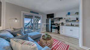 A modern living room with a large sofa, a coffee table, and a view of the beach through a sliding door.