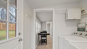 A laundry room with a washing machine, a drying rack, and a dining area with a table and chairs. - Bright & Cozy Bungalow Close To Downtown! Dogs Stay Free! (Hendersonville)