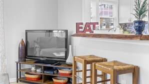 A living room with a television, two wicker bar stools, a wooden coffee table, and a decorative sign on the window sill. - Bright & Cozy Bungalow Close To Downtown! Dogs Stay Free! (Hendersonville)