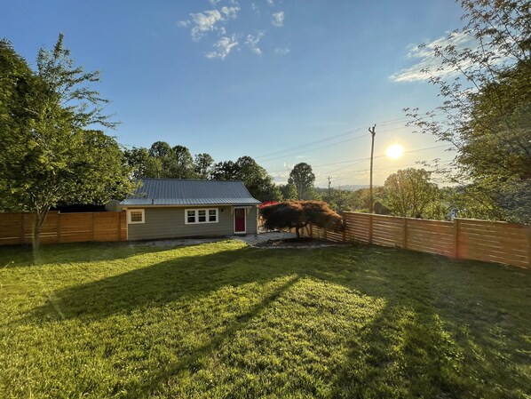 Uma casa com porta vermelha, cercada por uma vedação de madeira e um gramado bem cuidado.