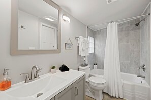 A modern bathroom with a white sink, a mirror, a toilet, and a shower with a curtain.