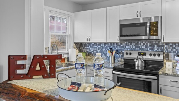 A modern kitchen with white cabinets, a stainless steel microwave, and a black stove. - Bright & Cozy Bungalow Close To Downtown! Dogs Stay Free! (Hendersonville)