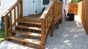 Una terraza de madera con escalones que conducen a una puerta blanca, una planta en maceta y una valla de madera.