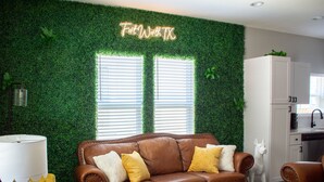 Una sala de estar con un sofá de cuero marrón, sillones amarillos, una mesa de centro de madera y una pared verde con un letrero de neón.