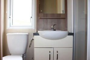 A compact bathroom with a white toilet, a sink with a mirror above it, and a cabinet below. - Glen View - mobile home with spectacular alpine and loch view (Taynuilt)