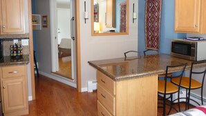 A compact kitchen with wooden cabinets, a microwave, and a small dining area with chairs. - Architect designed 1-bdrm/+wall-bed, 15-min walk to downtown, Patio/balcony/View (Estes Park)