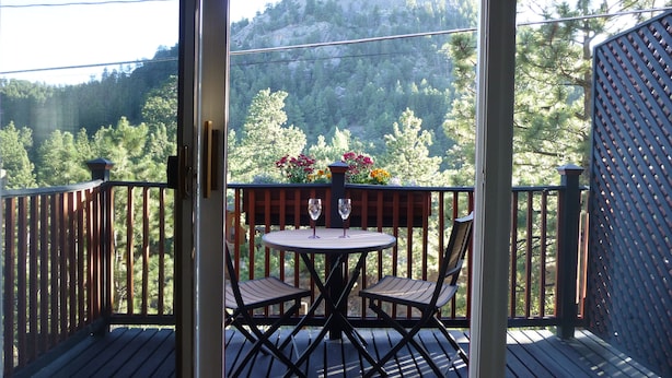 A wooden deck with a round table and two chairs, overlooking a forested area with a mountain in the background. - Architect designed 1-bdrm/+wall-bed, 15-min walk to downtown, Patio/balcony/View (Estes Park)