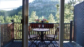 En träveranda med ett runt bord och två stolar, med utsikt över ett skogsområde och ett berg i bakgrunden.