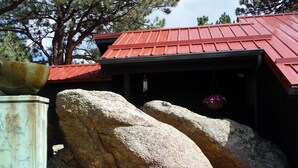 A building with a red roof, large rocks in front, and a hanging flower basket. - Architect designed 1-bdrm/+wall-bed, 15-min walk to downtown, Patio/balcony/View (Estes Park)