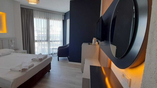 Habitación de hotel con una cama, un escritorio con televisor de pantalla plana, una silla y un espejo grande.