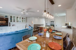 A modern kitchen with white cabinets, a blue accent wall, and a dining area with a wooden table set for six. - Mission Tides 2 | 3BR Mission Beach Rooftop Deck (San Diego)