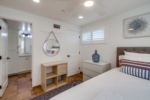 Quarto com cama, mesa de cabeceira, cômoda, espelho e janela com persianas.
