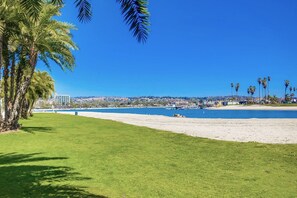 Una playa con zona verde, palmeras y vista al océano y edificios distantes.