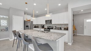 A modern kitchen with white cabinets, a granite countertop, and a central island with bar stools. - EV_8900 - 5BR / 4.5BA Villa w/ Private Pool, Game Room & Resort Access (Kissimmee)