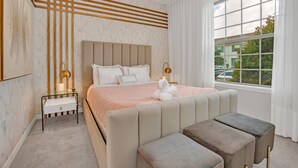 A modern bedroom with a large bed, bedside tables, a bench, and a window with a view of the outside. - EV_8900 - 5BR / 4.5BA Villa w/ Private Pool, Game Room & Resort Access (Kissimmee)