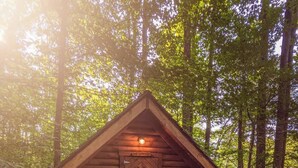 Eine kleine Holzhütte mit einer Fischschuppentür, umgeben von einem Wald.