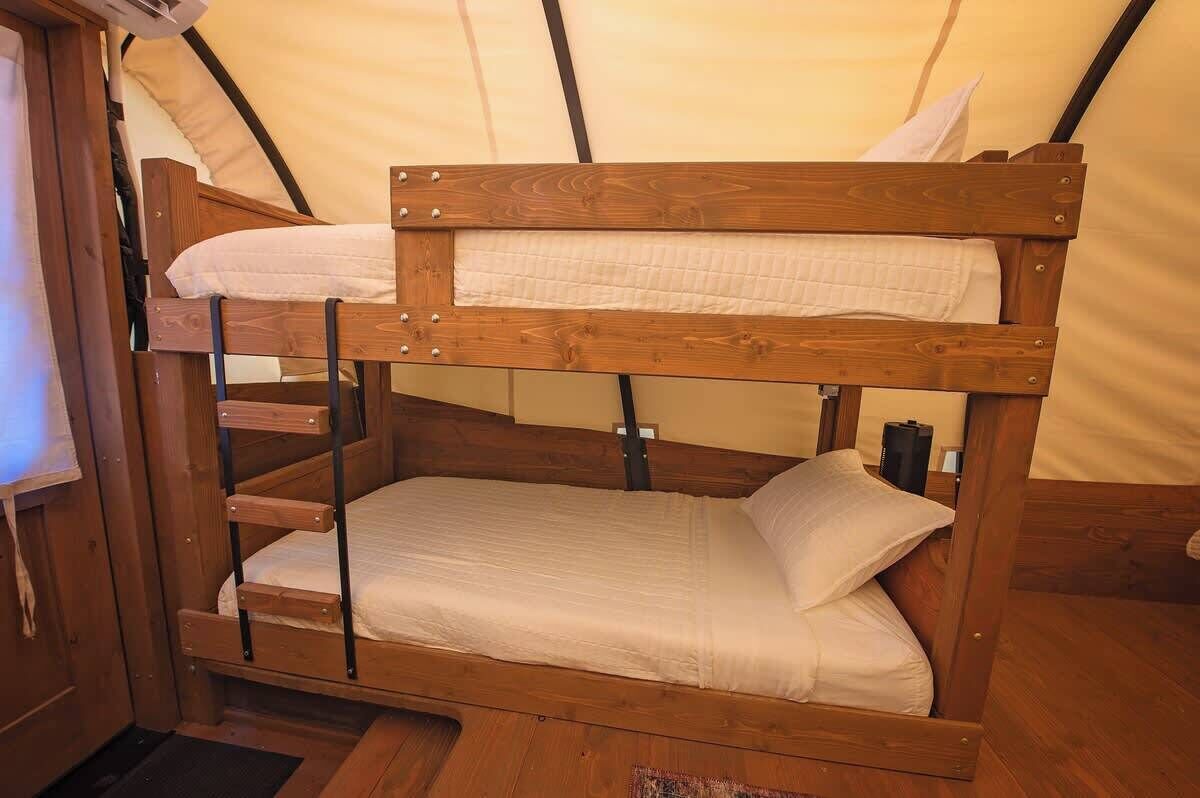 Una cama litera con estructura de madera y ropa de cama blanca dentro de una estructura similar a una tienda de campaña.