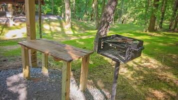 A wooden bench and a metal grill in a forested area.
