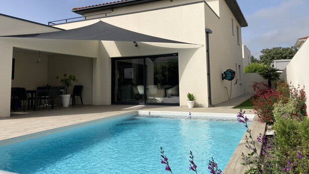 Een moderne woning met een zwembad, tuinmeubilair en een overdekt terras.
