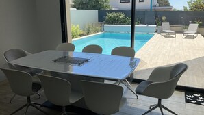 Een moderne kamer met een groot raam dat uitkijkt over een zwembad en een terras met buitenmeubilair.