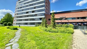 Um edifício moderno com vários andares, um caminho pavimentado e vegetação bem cuidada.