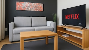 Uma sala de estar moderna com um sofá cinzento, uma mesa de centro de madeira e uma televisão de tela plana exibindo o logotipo da Netflix.