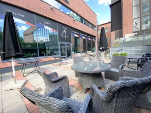 An outdoor seating area with wicker chairs and tables, a buffet sign, and a building with large windows. - TH City Suite 3 (Tampere)