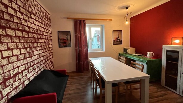 Un espace de vie compact doté d’un mur décoré d’un motif en briques, d’une table à manger, d’un canapé et d’un coin cuisine.