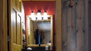 Une salle de bain en bois avec un meuble-lavabo, un miroir avec éclairage intégré et un mur d’accent rouge.