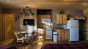 Une cuisine compacte avec des meubles en bois, un four à micro-ondes, une cuisinière et un réfrigérateur. On y trouve une table à manger avec des chaises, ainsi qu’un téléviseur fixé au mur.