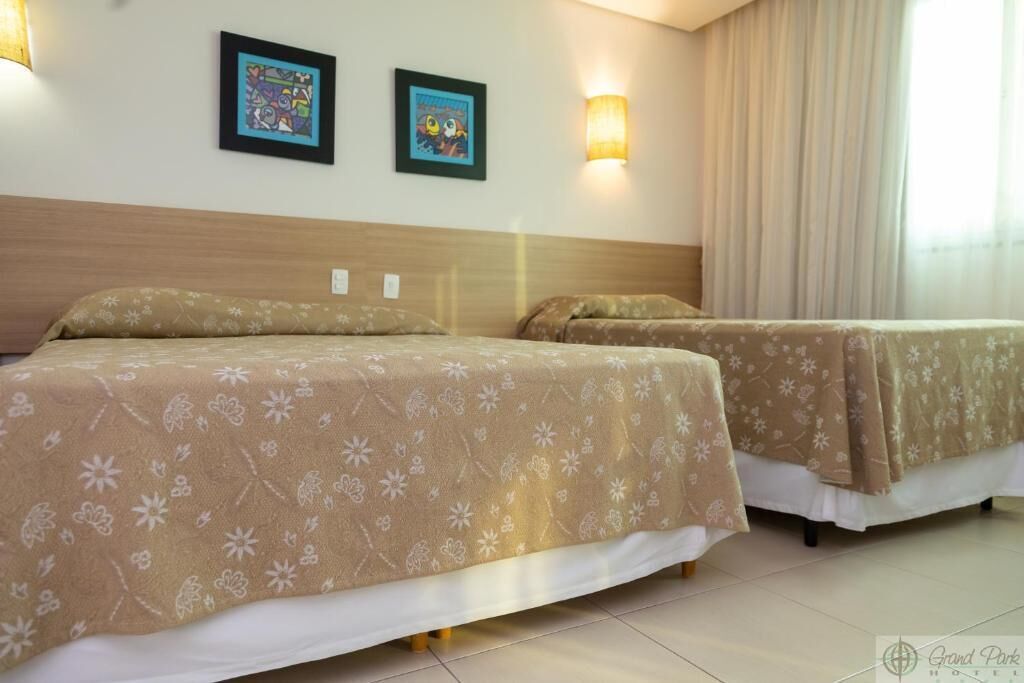 Habitación de hotel con dos camas, ropa de cama con estampado floral, dos cuadros en la pared y una lámpara en la mesita de noche.
