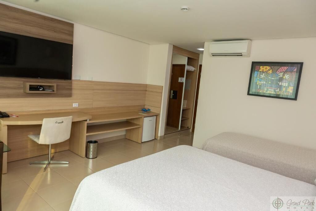 Habitación de hotel con cama, escritorio con silla, televisor y una pequeña kitchenette.