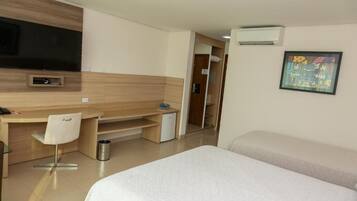 Habitación de hotel con cama, escritorio con silla, televisor y una pequeña kitchenette.