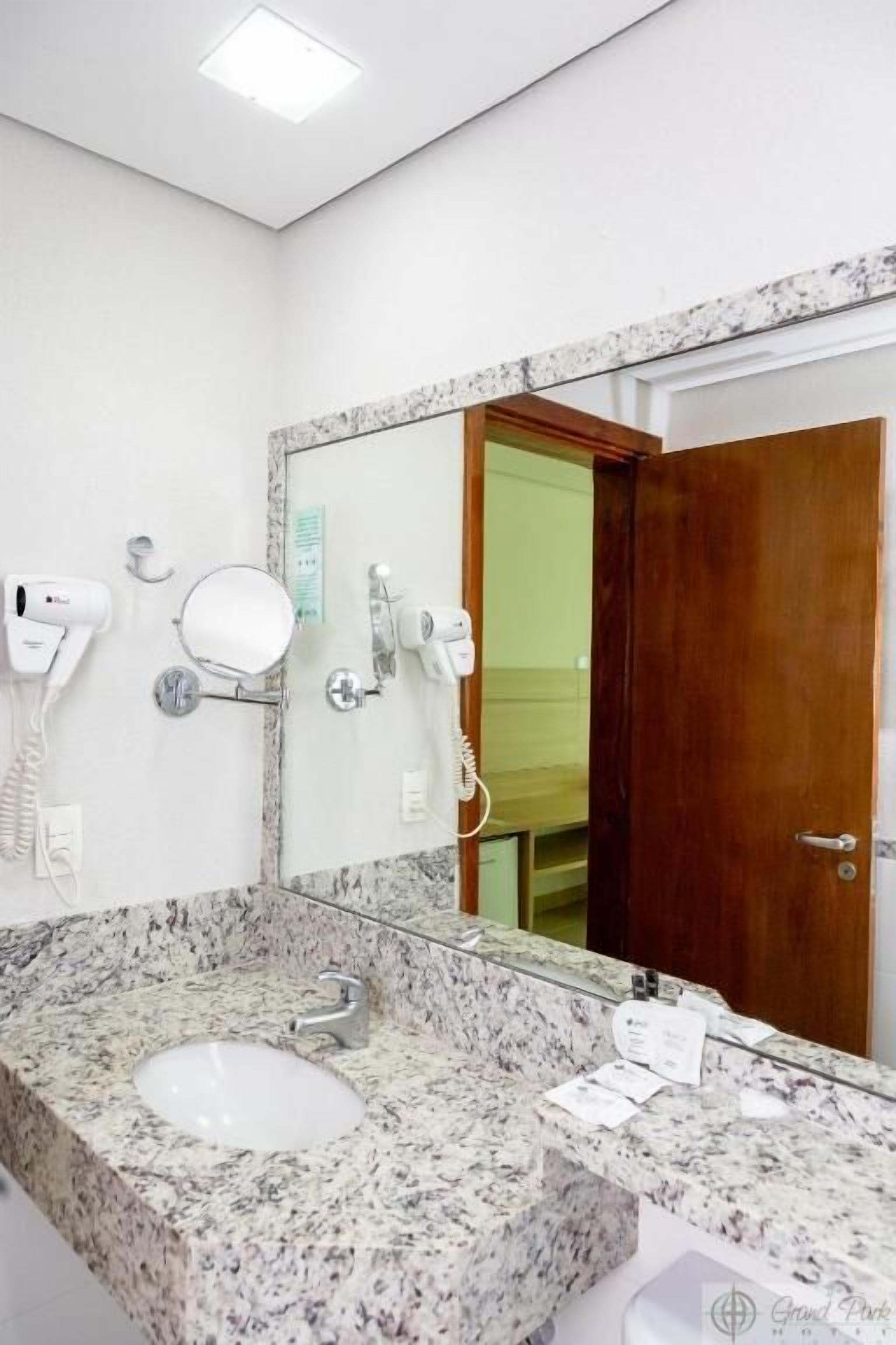 Un baño con lavamanos de encimera de granito, un espejo y dos secadores de pelo fijados en la pared.
